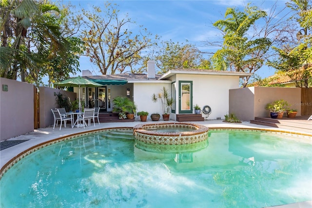 rear view of property with a patio, a chimney, fence, a pool with connected hot tub, and stucco siding