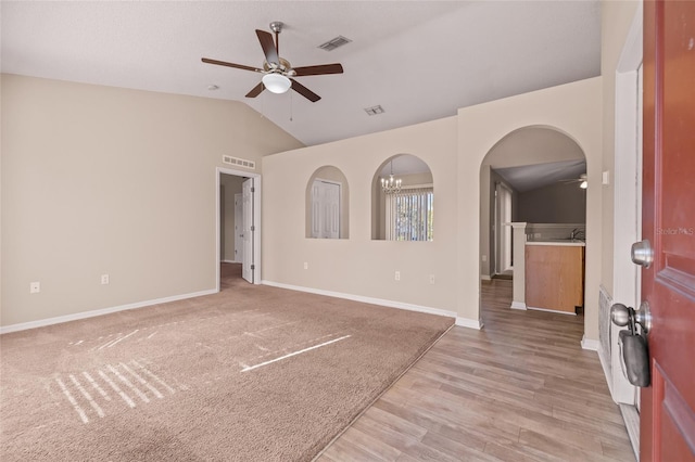 spare room with lofted ceiling, ceiling fan with notable chandelier, and light carpet