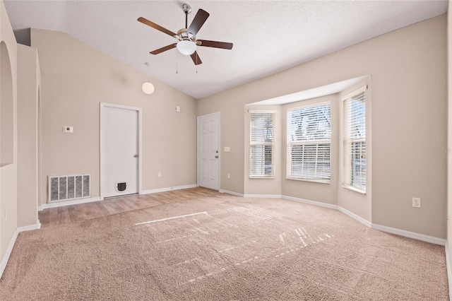 spare room featuring ceiling fan, vaulted ceiling, light carpet, and a textured ceiling