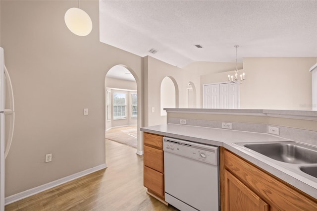 kitchen with vaulted ceiling, sink, hanging light fixtures, white dishwasher, and light hardwood / wood-style flooring