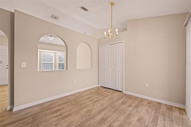 unfurnished room with an inviting chandelier, vaulted ceiling, a textured ceiling, and light wood-type flooring