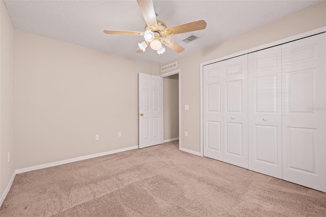 unfurnished bedroom featuring light carpet, a textured ceiling, a closet, and ceiling fan