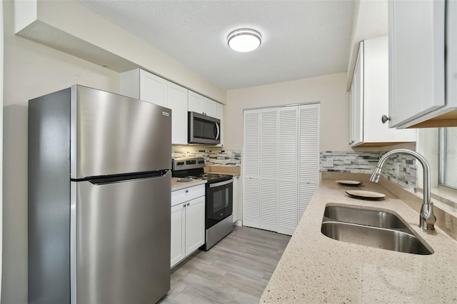 kitchen featuring sink, backsplash, stainless steel appliances, light stone counters, and white cabinets