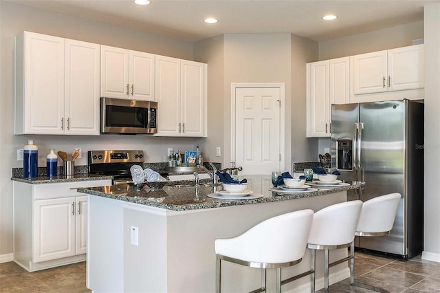 kitchen featuring dark stone countertops, stainless steel appliances, an island with sink, and white cabinets