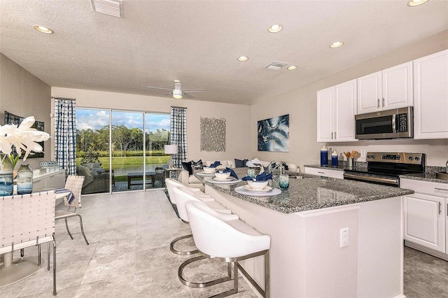 kitchen featuring appliances with stainless steel finishes, white cabinetry, a kitchen bar, a center island, and ceiling fan