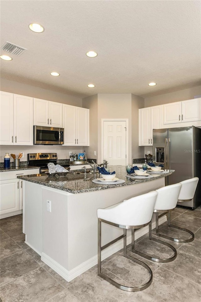 kitchen featuring a breakfast bar area, white cabinetry, a center island with sink, dark stone countertops, and appliances with stainless steel finishes