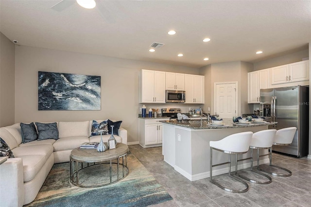 kitchen with appliances with stainless steel finishes, white cabinetry, sink, dark stone counters, and a center island with sink