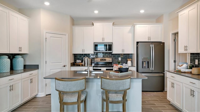 kitchen featuring white cabinetry, stainless steel appliances, and an island with sink