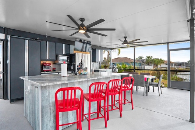 kitchen with a water view, a breakfast bar area, stainless steel appliances, light stone counters, and a spacious island