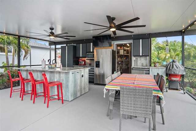 exterior space with an island with sink, ceiling fan, wine cooler, and light stone counters