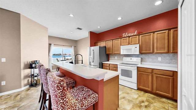 kitchen featuring a kitchen bar, sink, tasteful backsplash, white appliances, and a kitchen island with sink