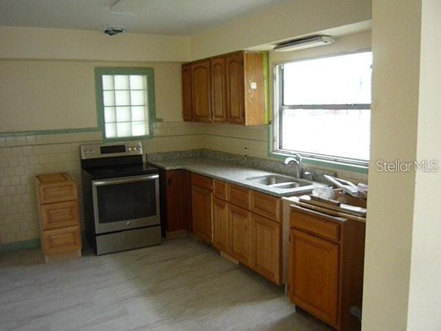 kitchen featuring tile walls, sink, stainless steel electric range, and light wood-type flooring