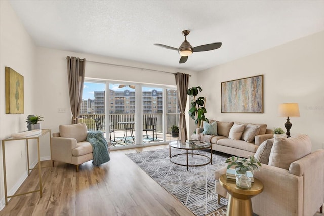 living room featuring ceiling fan, light hardwood / wood-style flooring, and a textured ceiling