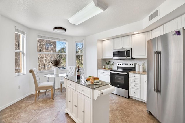 kitchen with white cabinetry, tasteful backsplash, light stone counters, a center island, and appliances with stainless steel finishes