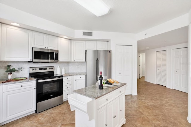 kitchen featuring a center island, appliances with stainless steel finishes, light stone countertops, decorative backsplash, and white cabinets