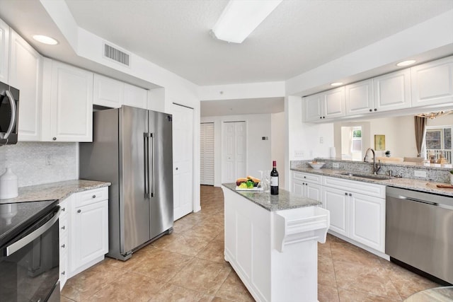 kitchen with stainless steel appliances, sink, white cabinets, and light stone counters