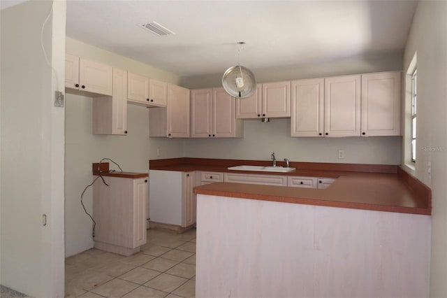 kitchen with a peninsula, light tile patterned flooring, a sink, and visible vents