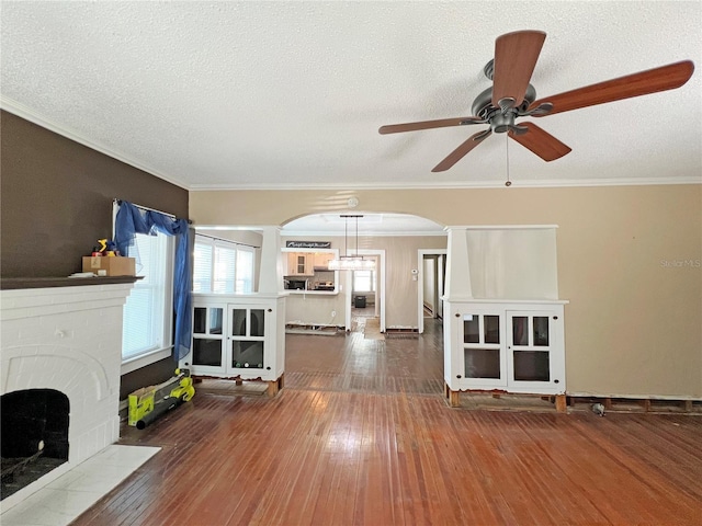 14124 Plum Ln, Hudson, FL 34667 - unfurnished living room featuring arched walkways, a ceiling fan, a brick fireplace, hardwood / wood-style floors, and crown molding
