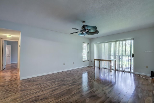 spare room featuring ceiling fan, a healthy amount of sunlight, dark hardwood / wood-style flooring, and a textured ceiling