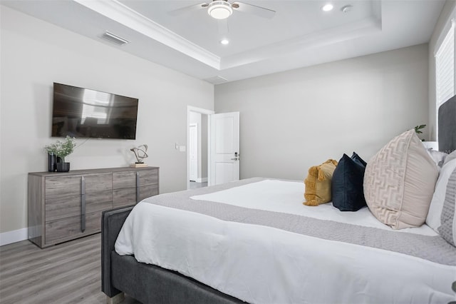 bedroom with ceiling fan, light wood-type flooring, and a tray ceiling