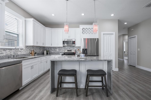 kitchen with appliances with stainless steel finishes, hanging light fixtures, a kitchen island, and white cabinets