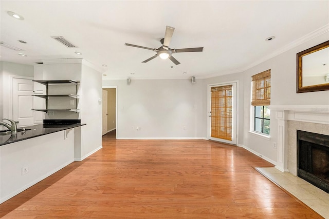 unfurnished living room with crown molding, a fireplace, light hardwood / wood-style floors, and ceiling fan