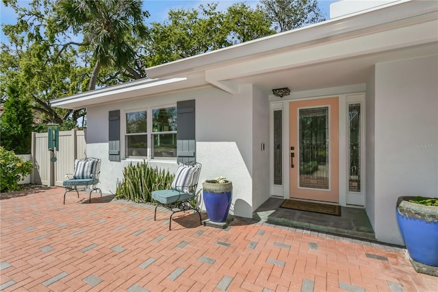 view of exterior entry with a patio, fence, and stucco siding