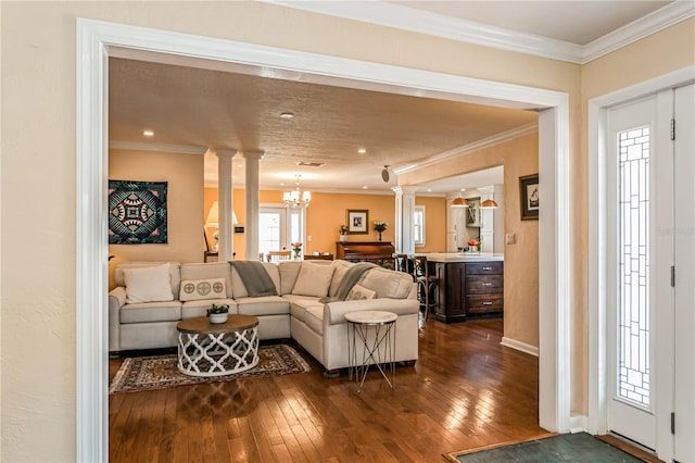 living area featuring decorative columns, baseboards, ornamental molding, dark wood-style flooring, and a notable chandelier