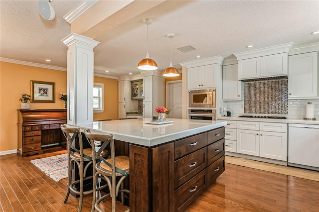 kitchen with appliances with stainless steel finishes, visible vents, decorative columns, and white cabinetry