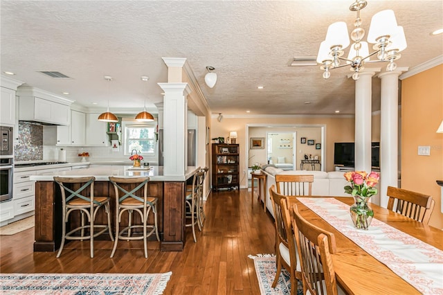 dining area featuring visible vents, ornamental molding, dark wood-style flooring, a textured ceiling, and ornate columns