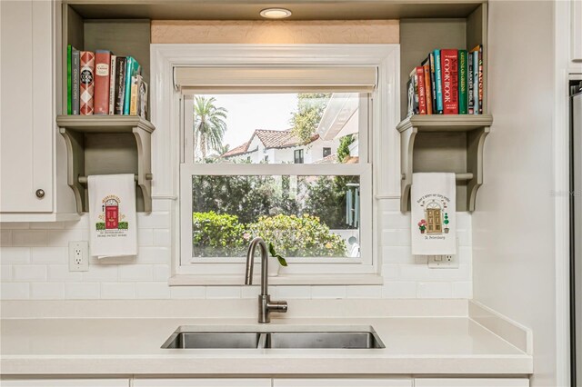 kitchen with tasteful backsplash, white cabinets, light countertops, and a sink