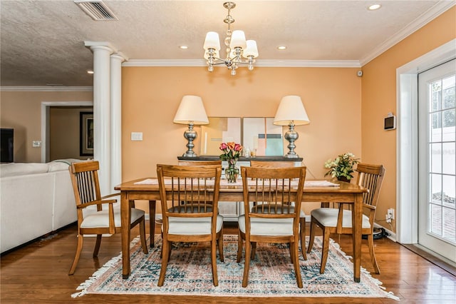 dining space with crown molding, wood-type flooring, visible vents, a textured ceiling, and ornate columns