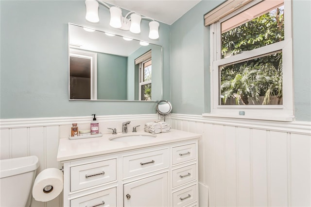 half bathroom with wainscoting, vanity, and toilet