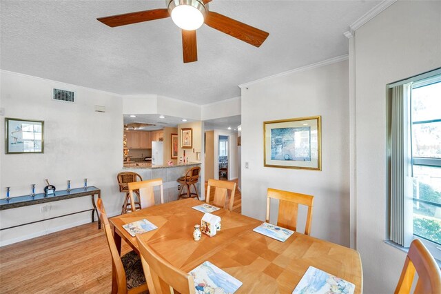 dining area featuring ornamental molding, visible vents, a textured ceiling, and light wood finished floors