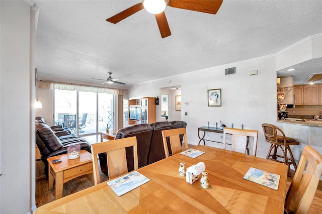 dining area featuring ornamental molding, visible vents, ceiling fan, and a textured ceiling