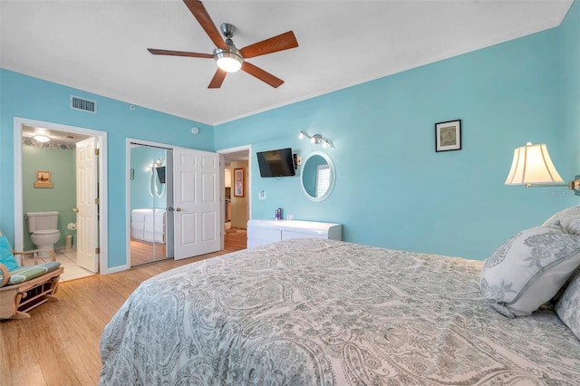 bedroom featuring ensuite bathroom, wood finished floors, visible vents, and a ceiling fan