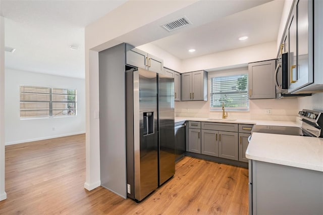 kitchen with gray cabinetry, sink, light hardwood / wood-style flooring, and stainless steel appliances