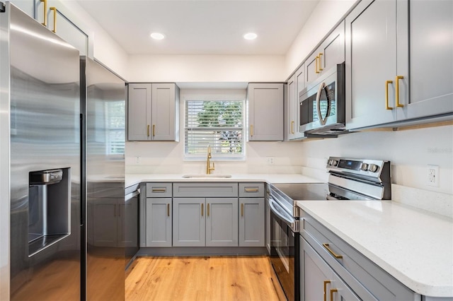 kitchen featuring light hardwood / wood-style floors, appliances with stainless steel finishes, gray cabinets, and sink