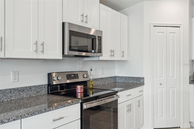 kitchen with stainless steel appliances, white cabinetry, and dark stone countertops