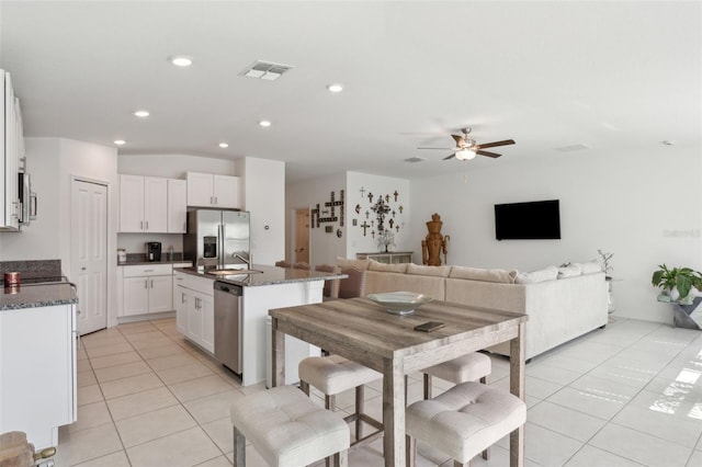 kitchen with visible vents, stainless steel appliances, light tile patterned flooring, white cabinetry, and a kitchen island with sink