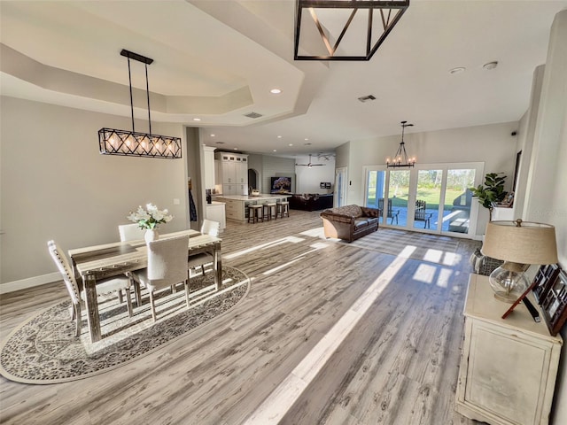 dining room with light wood finished floors, a raised ceiling, visible vents, a chandelier, and baseboards