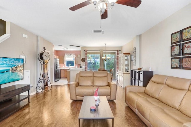 living room featuring ceiling fan with notable chandelier and light hardwood / wood-style floors