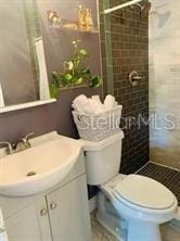 bathroom featuring vanity, a tile shower, and toilet