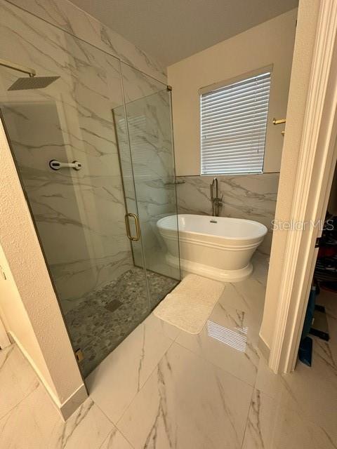 full bathroom with marble finish floor, a soaking tub, a marble finish shower, and tile walls