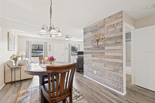 dining space featuring ceiling fan with notable chandelier, wooden walls, a textured ceiling, and light wood-type flooring