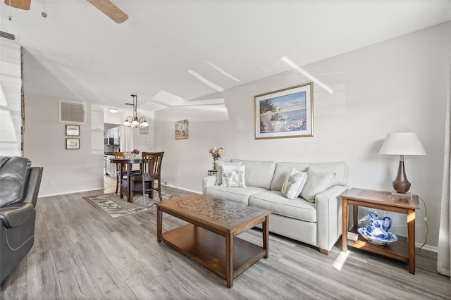 living room with ceiling fan with notable chandelier, a textured ceiling, and light wood-type flooring