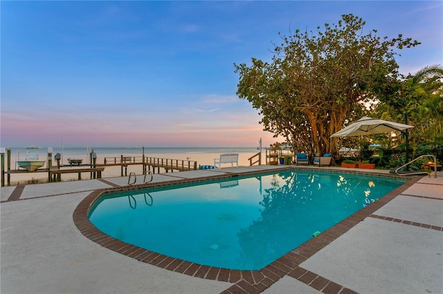 pool at dusk featuring a water view, a dock, and a patio area