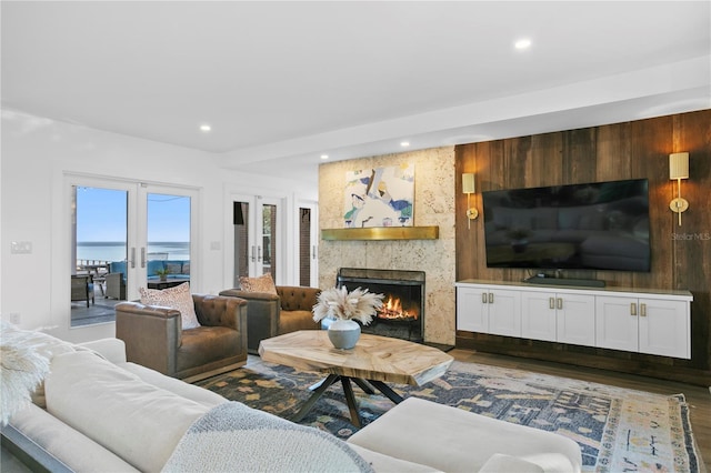 living room with french doors, dark wood-type flooring, a large fireplace, and a water view