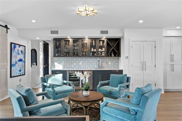 living room featuring a barn door, beverage cooler, wet bar, and light wood-type flooring