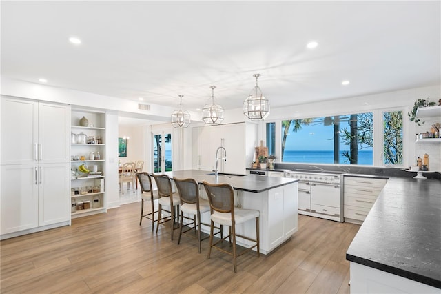 kitchen featuring a kitchen bar, sink, white cabinetry, hanging light fixtures, and a kitchen island